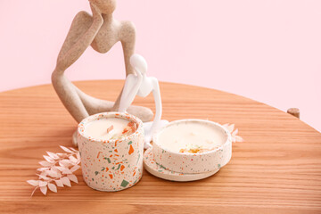 Holders with candles and decor on table near pink wall in room