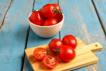 Board and bowl with fresh cherry tomatoes on blue wooden background