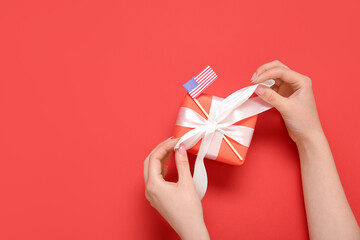 Woman tying bow on gift for American Independence Day with USA flag on red background