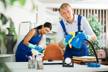 Portrait of professional worker of office cleaning service wiping furniture with rag and detergent...