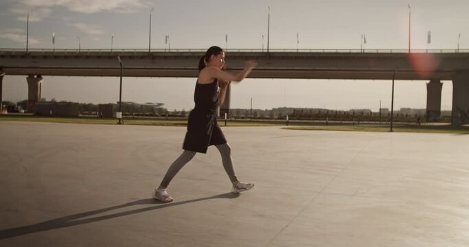 Strong sportswoman shadowboxing in morning sunlight in city