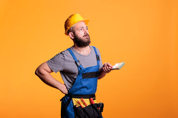 Confident handyman holding paintbrush to color walls, working on refurbishment project and painting...