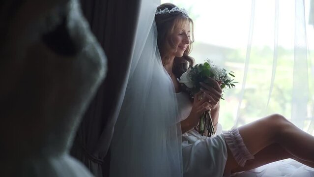 Close up shot of a sexy bride in petticoat putting on a garter near a window