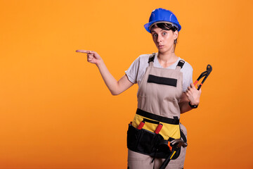 Woman builder indicating direction on left side of studio, posing with pair of pliers and pointing...