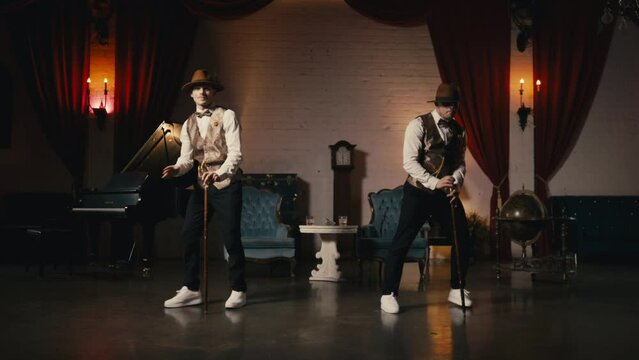 Music video, night show or event 4K. Two guys in dandy style outfit synchronically dancing in retro theatre stage. Classy male dancers performing in jazz funk style, dancing with classic cane in hands