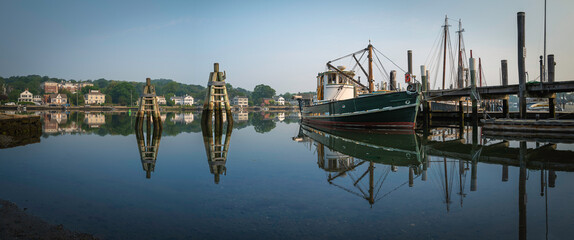 Mystic River summer landscape in Connecticut with moored trawler, commercial dock, piers, and water...