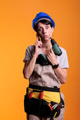 Bored construction worker answering smartphone call, posing over yellow background. Woman working as professional builder with power drilling gun, talking on mobile phone line.