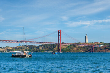 View of 25 de Abril Bridge famous tourist landmark over Tagus river, Christ the King monument and a tourist yacht boat. Lisbon, Portugal