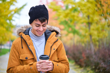 Smiling young man holding a cup of coffee on a cold autumn day.
