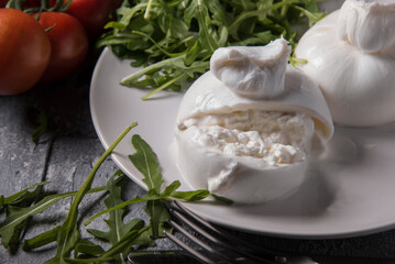 Cut Burrata cheese on a white plate with arugula and cherry tomatoes on a marble table, close up.