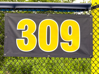 309 foot ft baseball field distance sign in yellow and black mounted on the black vinyl outfield fence.
