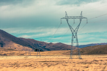 Photograph of large transmission towers and lines running through a valley against a blue sky on...