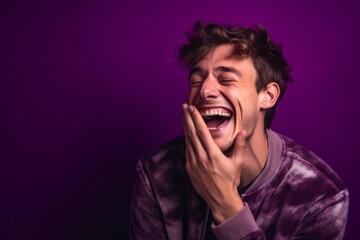 Fototapeta premium Close-up portrait photography of a satisfied boy in his 30s placing the hand over the mouth in a laughter gesture against a vibrant purple background. With generative AI technology
