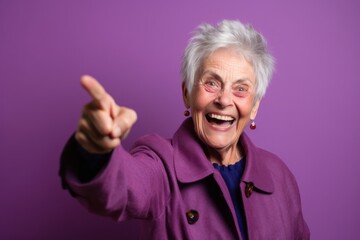 Close-up portrait photography of a grinning mature woman raising a finger as if having an idea against a vibrant purple background. With generative AI technology