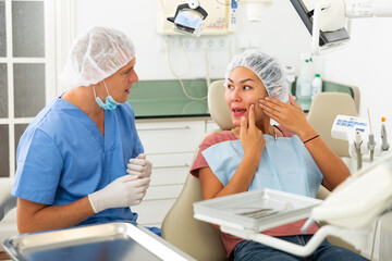 Woman patient sitting in a dental chair tells the dentist about her problem, showing which side she has a toothache