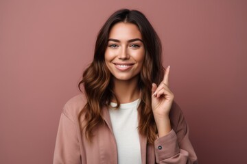 Fototapeta premium Headshot portrait photography of a tender girl in her 30s making a peace gesture with two fingers against a dusty rose background. With generative AI technology