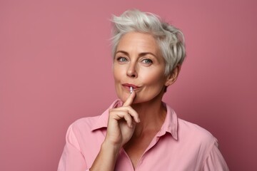 Medium shot portrait photography of a satisfied mature woman making a shhh gesture with a finger on the lips against a dusty rose background. With generative AI technology