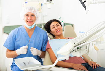 Portrait of a smiling man dentist with a positive woman patient sitting in a dental chair in the clinic office