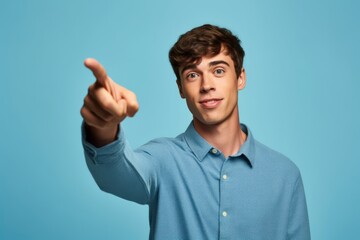 Medium shot portrait photography of a glad boy in his 20s pointing up against a soft blue background. With generative AI technology