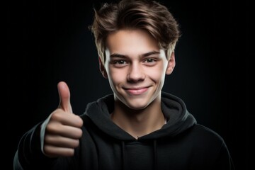 Naklejka premium Close-up portrait photography of a glad boy in his 20s showing a thumb up against a dark grey background. With generative AI technology
