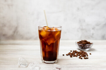 Ice coffee in a tall glass. Cold summer drink on a wooden background with copy space.