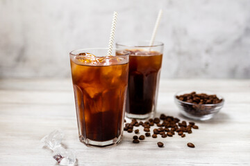 Ice coffee in a tall glass. Cold summer drink on a wooden background with copy space.
