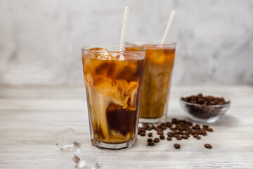 Ice coffee in a tall glass with milk. Cold summer drink on a wooden background with copy space.