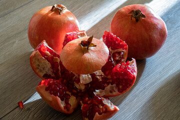 Two fresh ripe pomegranates and one cut on a gray wooden table. Close-up