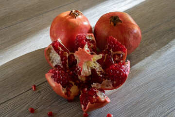 Two fresh ripe pomegranates and one cut on a gray wooden table. Close-up