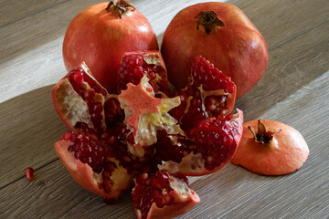 Two fresh ripe pomegranates and one cut on a gray wooden table. Close-up