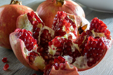 Two fresh ripe pomegranates and one cut on a gray wooden table. Close-up