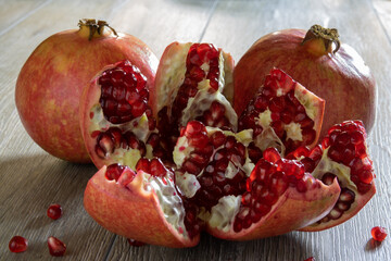 Two fresh ripe pomegranates and one cut on a gray wooden table. Close-up