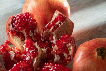 Two fresh ripe pomegranates and one cut on a gray wooden table. Close-up
