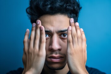 Headshot portrait photography of a tender boy in his 20s making a sorry gesture with hands together against a sapphire blue background. With generative AI technology