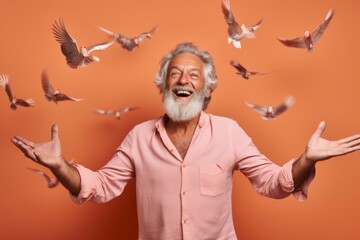 Medium shot portrait photography of a grinning mature man imitating the flight of a bird with the hands against a coral pink background. With generative AI technology