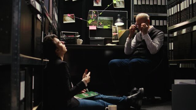 Stressed detectives working on case, trying to solve mystery and catch killer in incident room. Police agents team examining surveillance footage to identify culprit, gather intelligence.