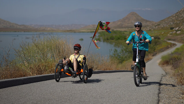 Mother and daughter biking up a hill next to a lake with mountains riding recumbent and normal electric bikes.