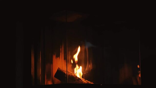 Burning fireplace in a dark room. Warm cozy home atmosphere. flame behind the glass of the fireplace. High quality 4k footage