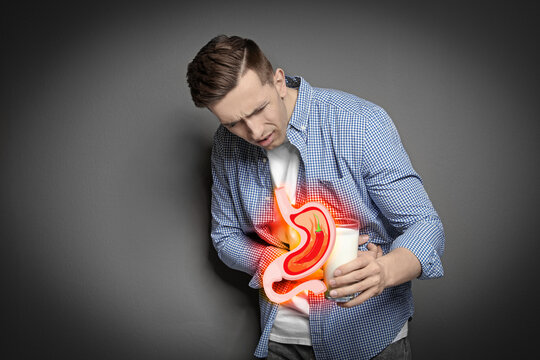 Man with glass of milk suffering from heartburn on grey background. Stomach with hot chili pepper symbolizing acid indigestion, illustration