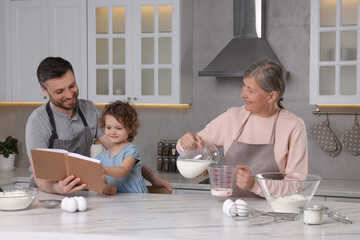 Cute little girl with her father and grandmother cooking by recipe book in kitchen