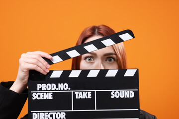 Emotional actress with clapperboard on orange background. Film industry