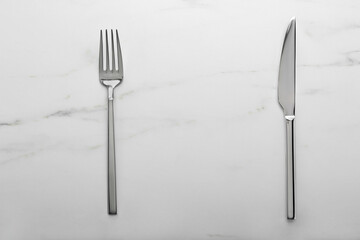 Shiny fork and knife on white marble table, flat lay. Space for text