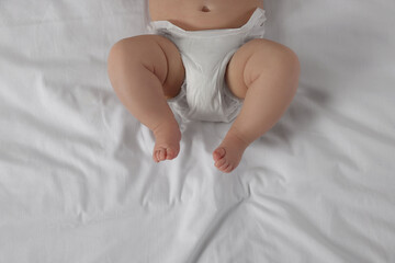 Little baby in diaper lying on bed, top view