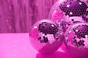 Shiny disco balls on table against blurred background, toned in pink. Space for text