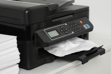 Modern printer with crumpled sheet of paper on white table