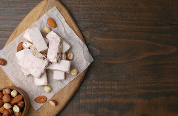 Pieces of delicious nutty nougat, hazelnuts and almonds on wooden table, top view. Space for text