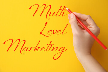 Woman writing text Multi Level Marketing on yellow background, closeup