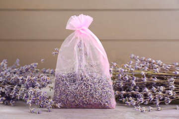 Scented sachet and dried lavender flowers on wooden table, closeup
