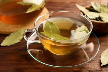 Cup of freshly brewed tea with bay leaves on wooden table, closeup