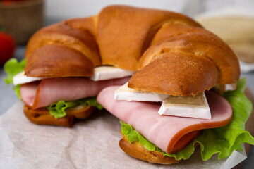 Tasty crescent roll with brie, ham and lettuce on parchment paper, closeup